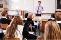 School classroom with teacher at front and children facing the board.