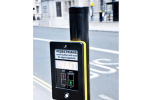 Pedestrian crossing push button mounted on a roadside pole, which is topped with a black plastic protective cap.