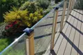 Raised decked balcony with glass panel railing overlooking a garden, featuring square plastic protective caps on the wooden balcony posts.