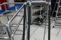 Black foam sleeves being applied to metal tubular frames in an industrial setting for protective or ergonomic purposes on handling equipment.