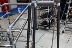 Black foam sleeves being applied to metal tubular frames in an industrial setting for protective or ergonomic purposes on handling equipment.