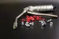 Grease gun with metal grease nipples and red protective caps displayed on a black surface.
