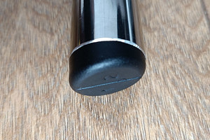 Angled top-down view of a round black LDPE injection-moulded foot insert fitted to the end of a metal tube leg, with an angled base profile visible.