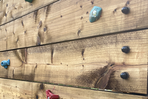 A wooden climbing wall with black LDPE nut caps mounted over hexagonal bolt heads.