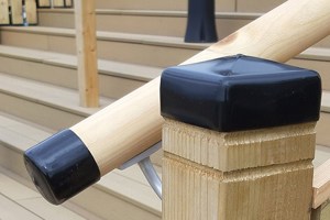 Close-up of a square wooden post and attached wooden bannister, both fitted with black plastic protective caps—one square and one round.
