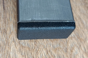 Top-down view of a black rectangular injection-moulded foot insert fitted to the base of a metal tube leg.